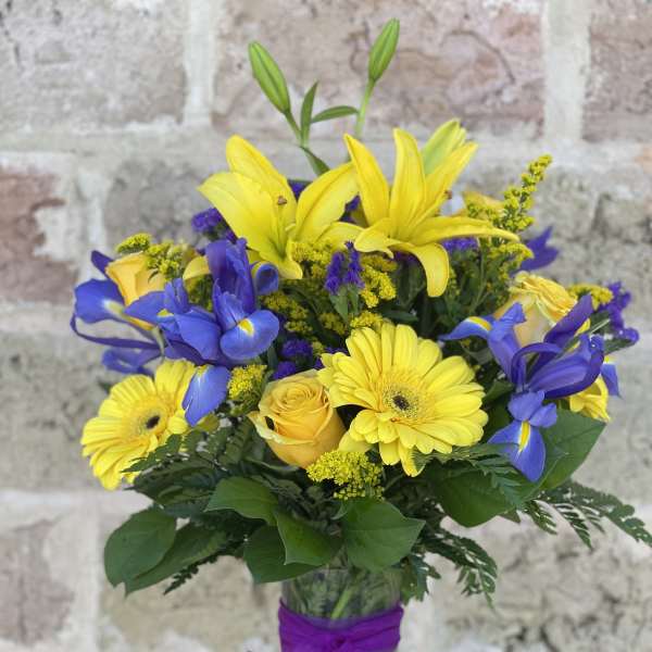 Yellow lilies, blue irises, and yellow daisies in a glass vase