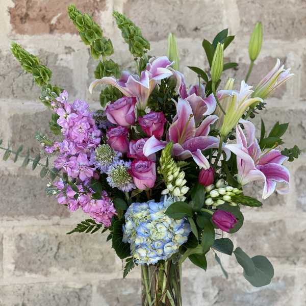 Mixed bouquet of pink lilies, roses, hydrangea, and lavender flowers in a glass vase
