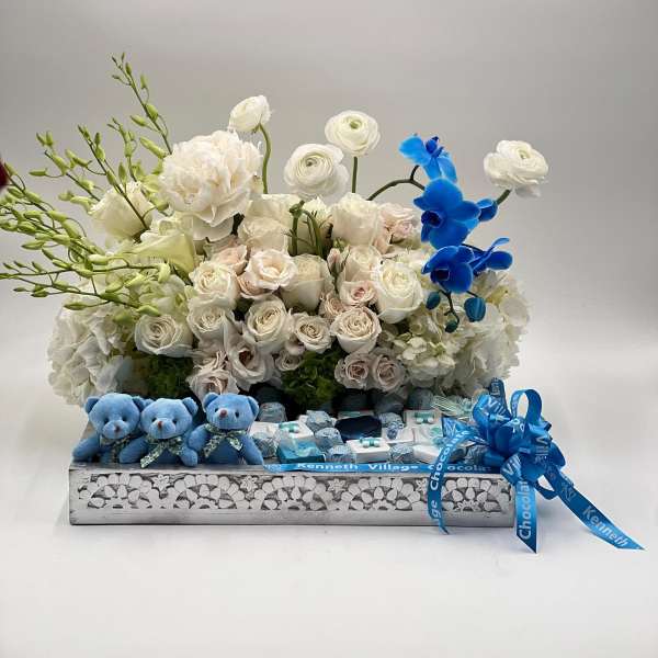 White rose arrangement with blue orchids and small teddy bears in a gift box