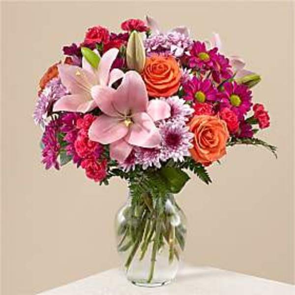 Bouquet of pink lilies, roses, and daisies in a clear glass vase