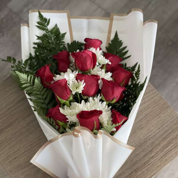 Bouquet of red roses and white daisies wrapped in white paper with a red bow