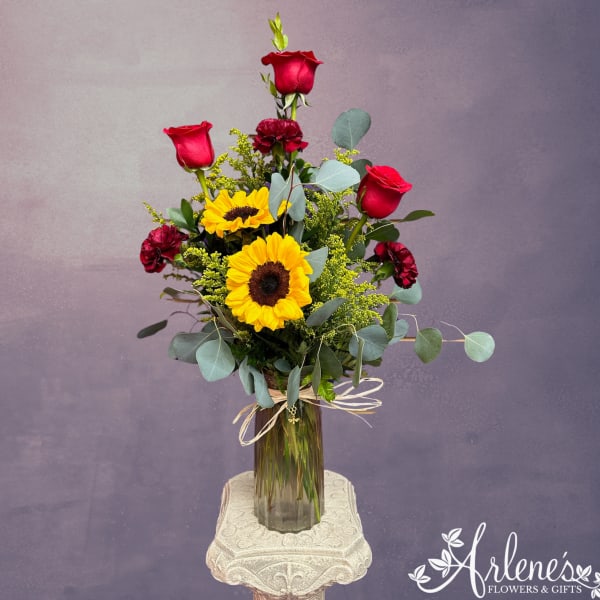 Tall bouquet of red roses and yellow sunflowers in a glass vase