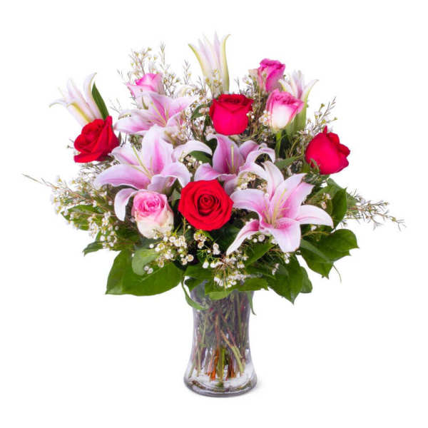 Glass vase arrangement with pink lilies, red and pink roses, and small white filler flowers