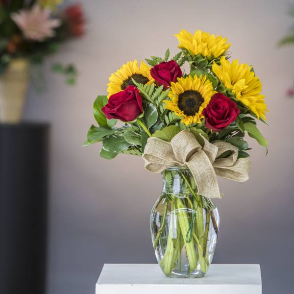 Sunflowers and red roses in a clear glass vase with a burlap bow