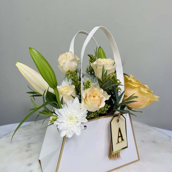 Cream roses and white lilies in a white gift bag with a letter tag