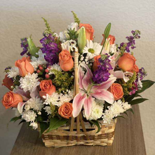 Basket arrangement of orange roses, pink lilies, and white daisies
