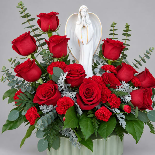 Red roses and carnations arranged around a white angel figurine in a vase