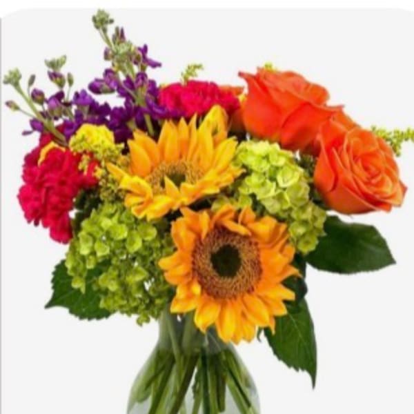 Colorful bouquet with sunflowers, roses, hydrangeas, and purple blooms in a glass vase
