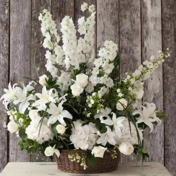White floral arrangement in a wicker basket with lilies and roses