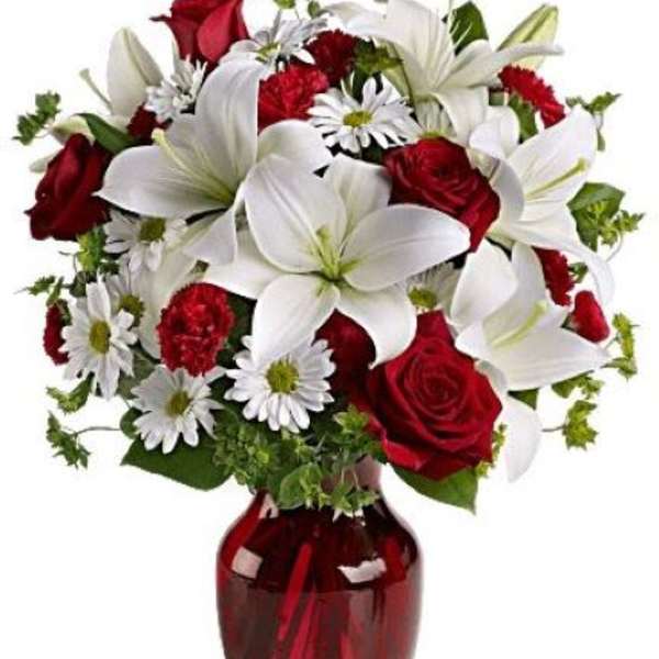 Arrangement of white lilies, red roses, red carnations, and white daisies in a red glass vase