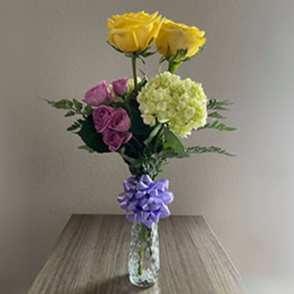 Bouquet of yellow and pink roses with a green hydrangea in a glass vase
