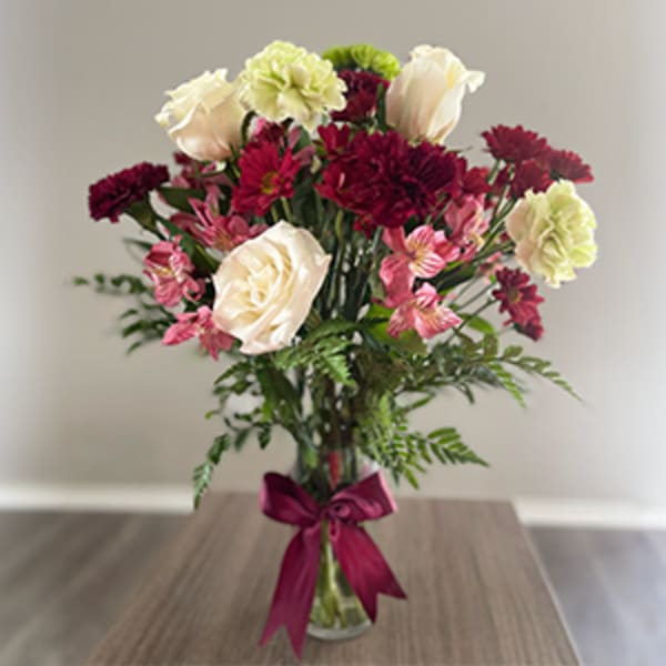 Bouquet of cream, pink, and burgundy flowers in a glass vase with a ribbon