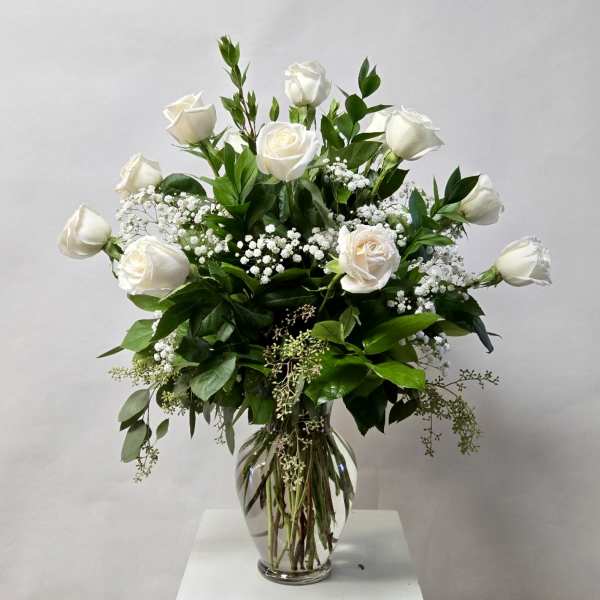 White roses in a clear glass vase with baby's breath and greenery