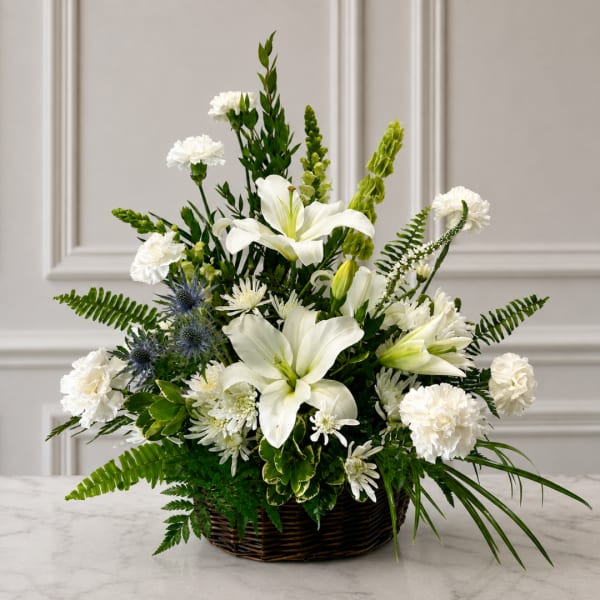 White lilies and carnations in a wicker basket with mixed greenery