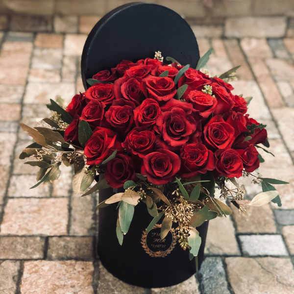 Red rose bouquet in a black hatbox with greenery
