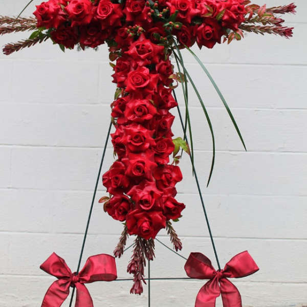 Red rose cross-shaped funeral spray on a stand with ribbon bows