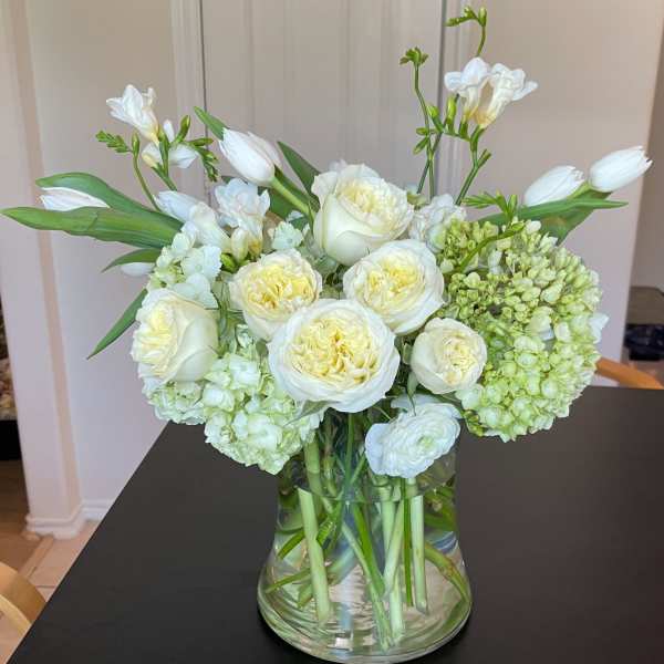 White roses and tulips arranged in a clear glass vase