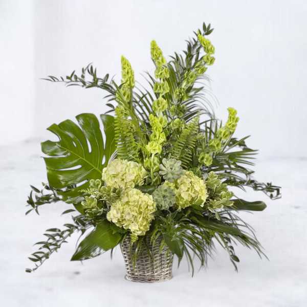 Green floral arrangement in a woven basket with hydrangeas and tropical leaves