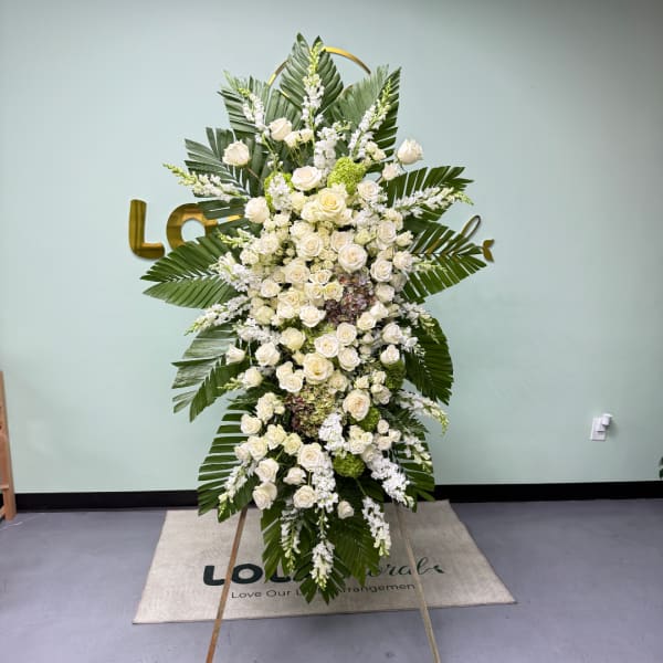 Tall standing floral spray with white roses and palm leaves on an easel