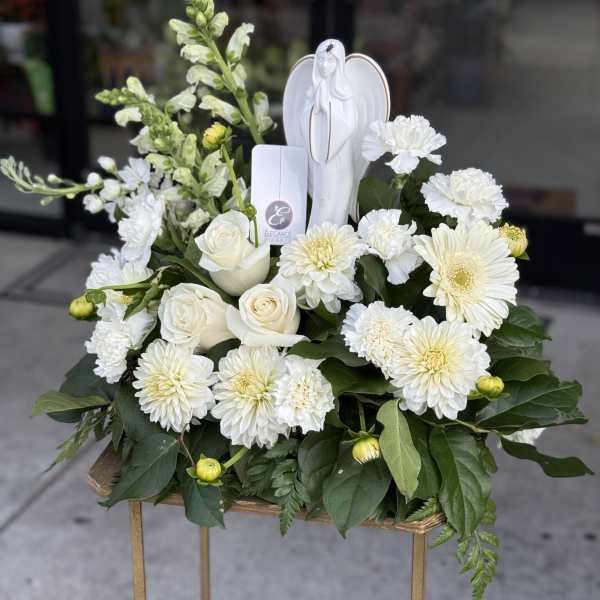 White floral sympathy arrangement with roses, chrysanthemums, and an angel figurine