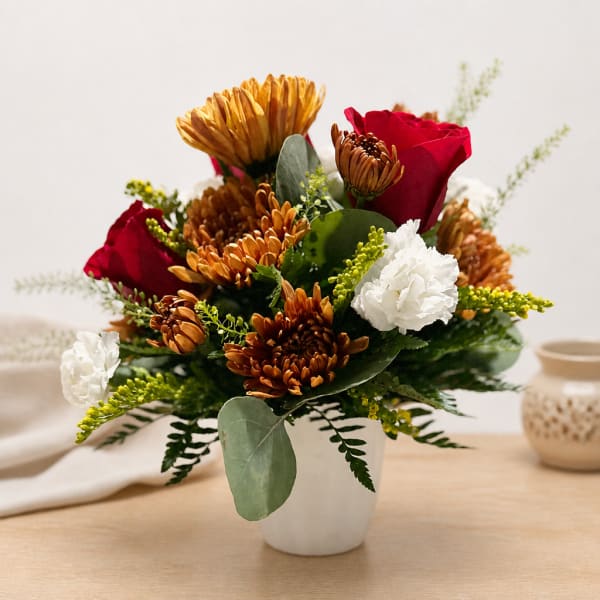 Bouquet of red roses, white carnations, and bronze chrysanthemums in a white vase.