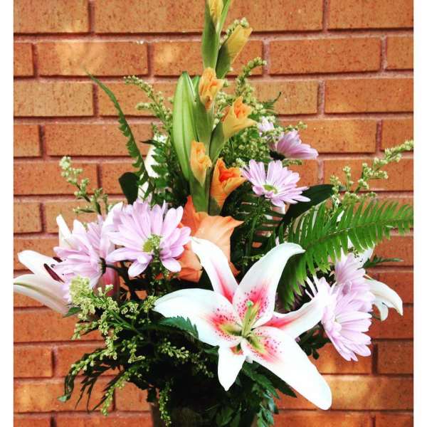 Tall arrangement with white lilies, peach gladiolus, and light purple daisies in a vase