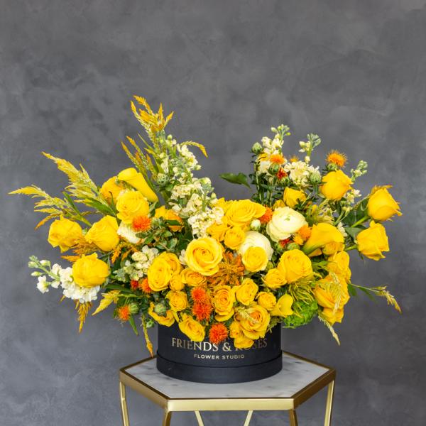 Yellow roses and white flowers arranged in a black hat box