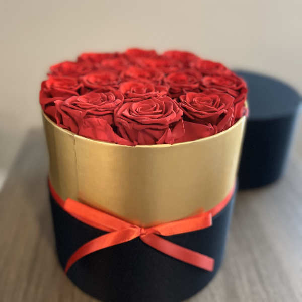 Red roses arranged in a round gold box with a red ribbon