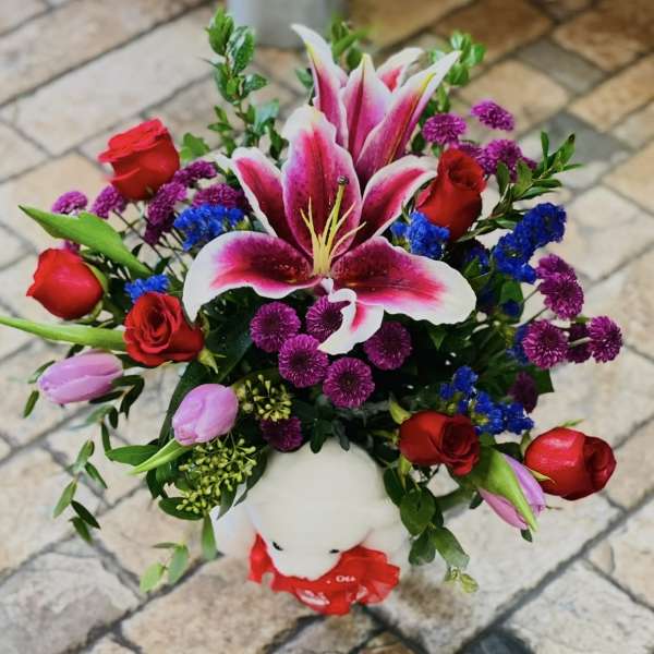 Bouquet of red roses, pink lilies, and purple flowers in a white teddy bear vase