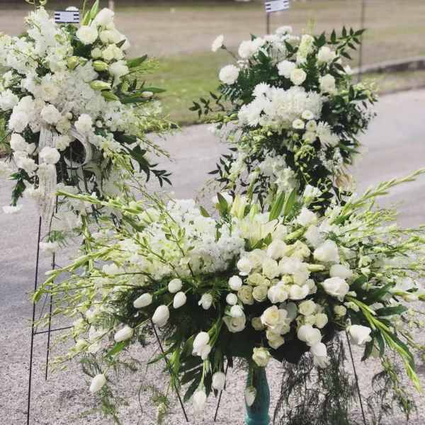White floral funeral sprays with lilies and roses on stands