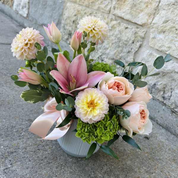 Pink lilies and peach roses in a white vase with a satin ribbon