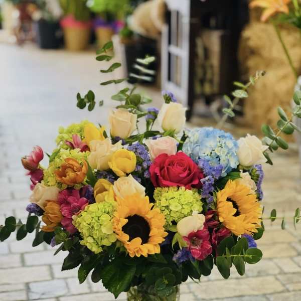 Mixed bouquet of sunflowers, roses, and hydrangeas in a clear glass vase