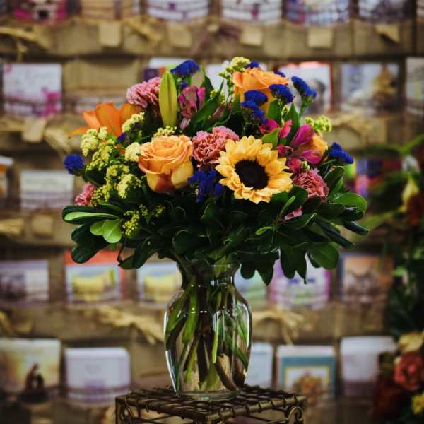 Mixed bouquet of orange, pink, yellow, and blue flowers in a glass vase