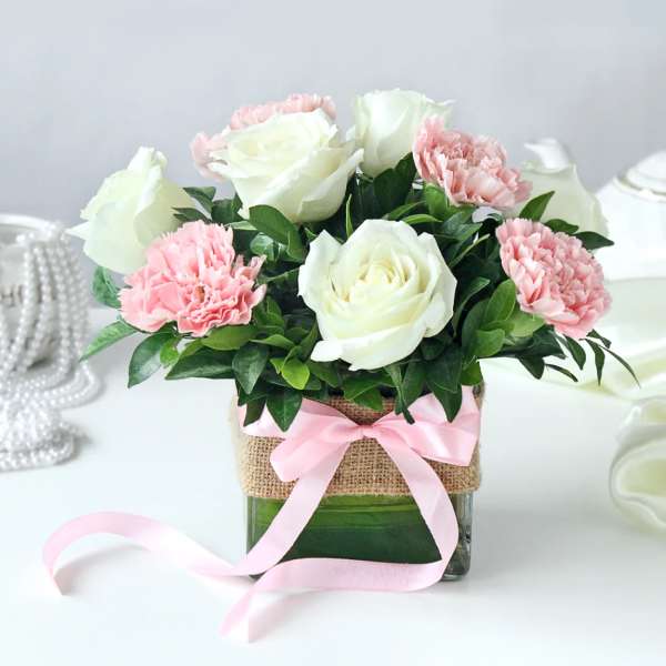 Pink carnations and white roses in a glass vase with a pink ribbon