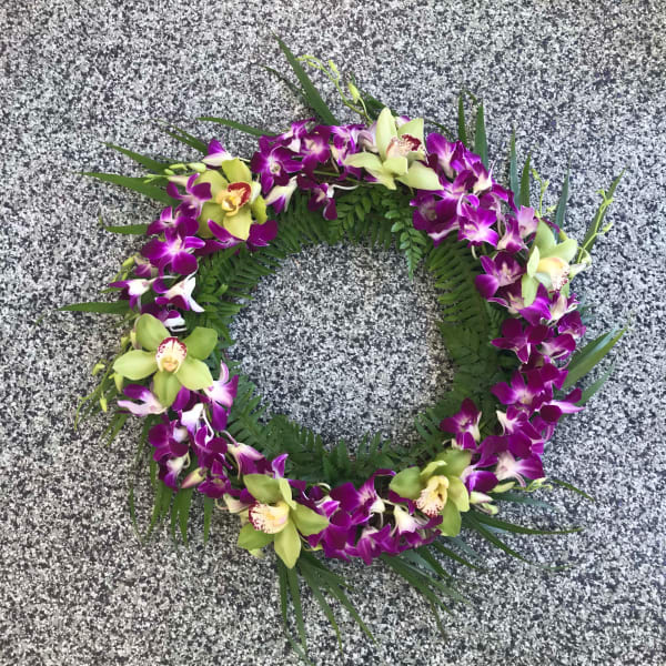 Circular orchid wreath with purple and green blooms on a stone surface