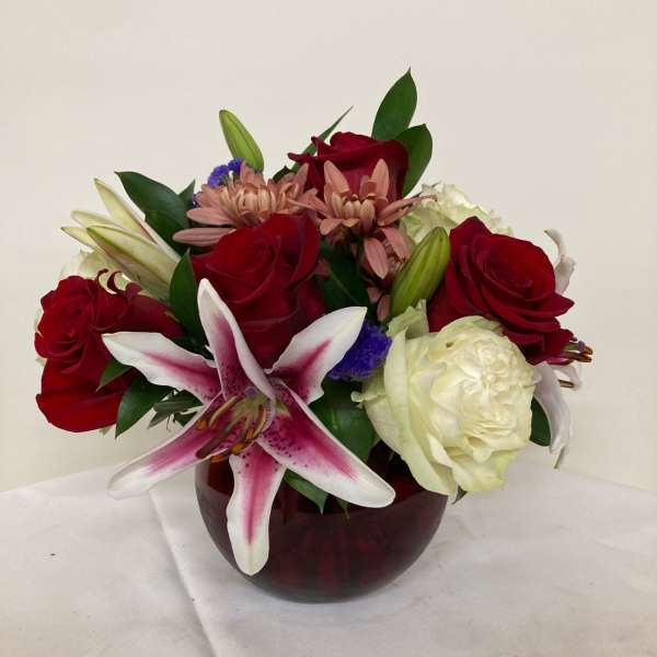 Mixed bouquet of red roses, white lilies, and pink flowers in a red glass vase