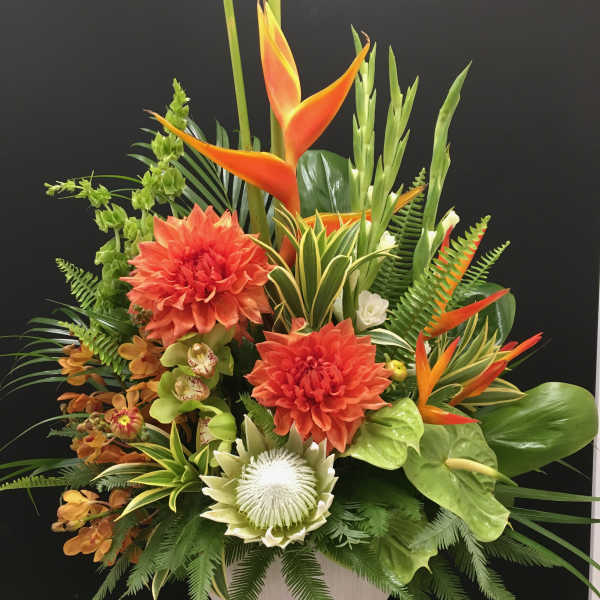 Tropical floral arrangement with orange blooms in a white vase