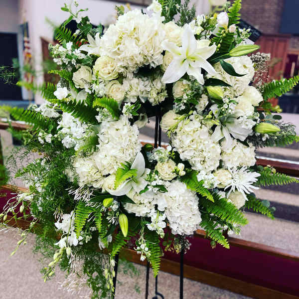 White floral standing spray with lilies, roses, and hydrangeas