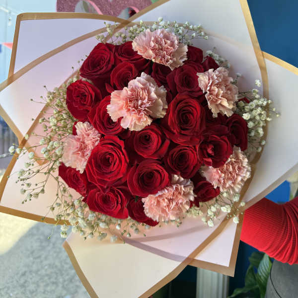 Bouquet of red roses and pale pink carnations wrapped in white paper