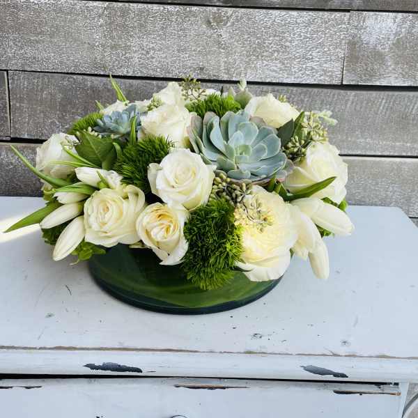 White roses and succulents arranged in a low green bowl