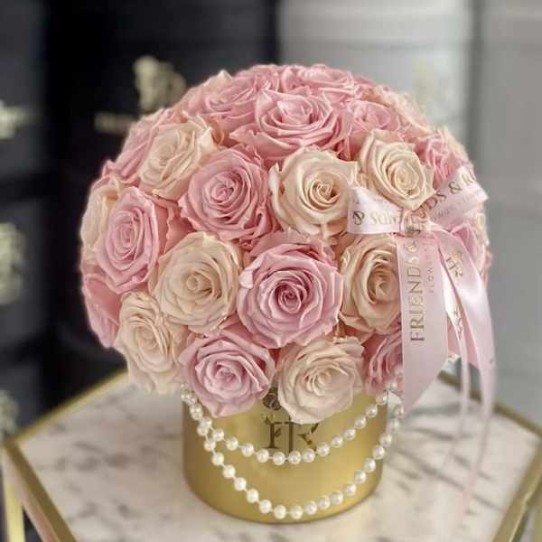 Pink and cream roses arranged in a gold hatbox with pearl strands