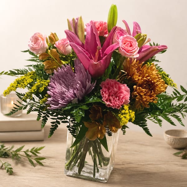 Mixed bouquet of pink lilies, roses, and chrysanthemums in a clear glass vase