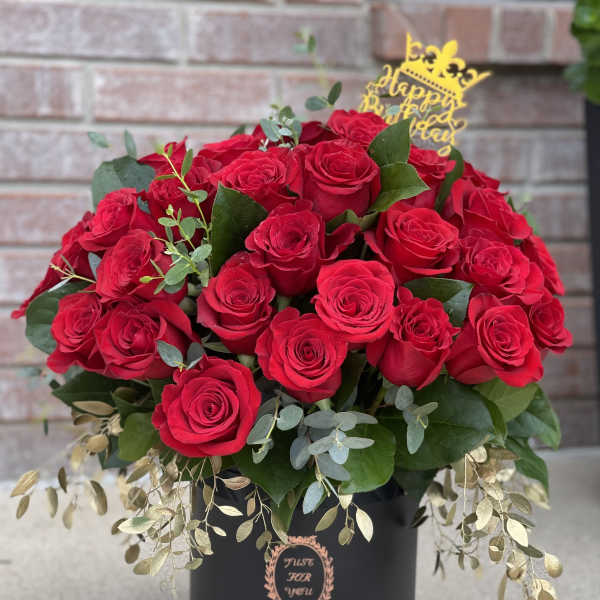 Red roses arranged in a black hatbox with a gold birthday topper