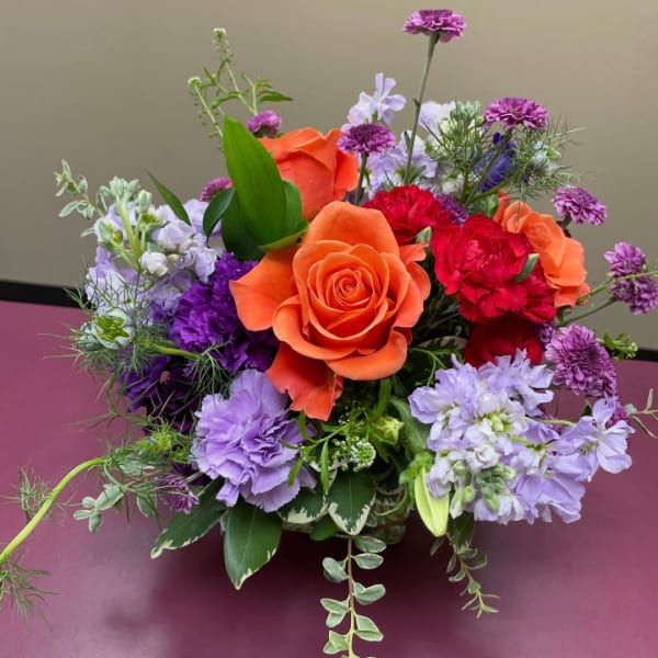Orange roses and purple flowers in a low bouquet