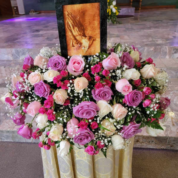 Large pink and white rose arrangement around a framed religious image