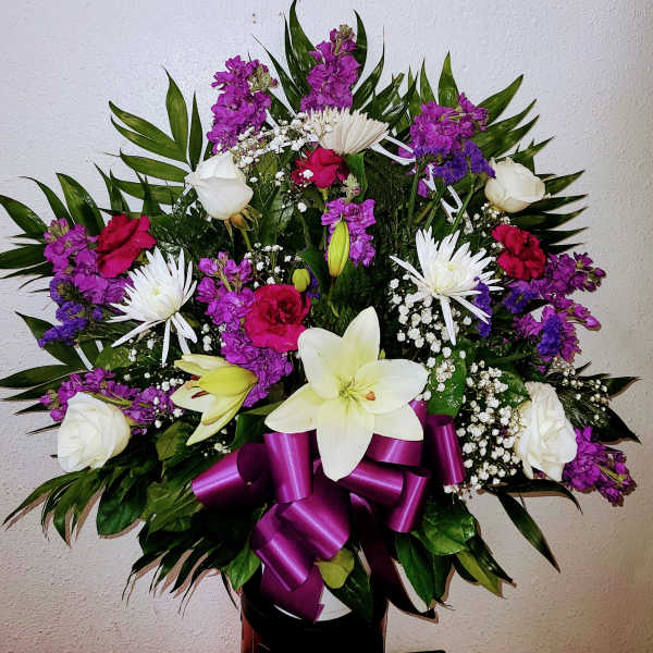Bouquet of white lilies, roses, and purple flowers with a magenta ribbon