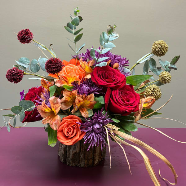 Mixed bouquet of red, orange, and purple flowers in a rustic vase