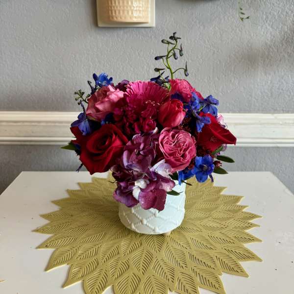 Colorful bouquet of roses, hydrangea, and blue flowers in a white vase