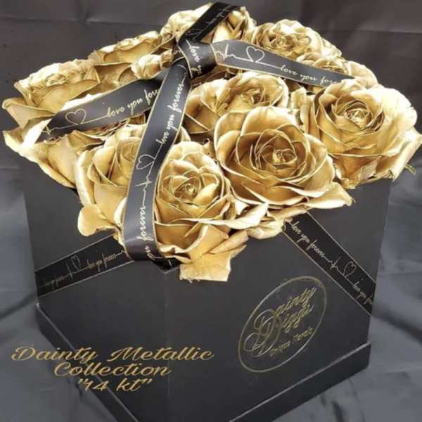 Gold roses arranged in a black gift box with a ribbon.
