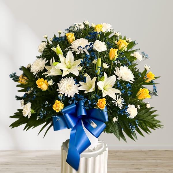 Large bouquet of white lilies, yellow roses, and white chrysanthemums with a blue ribbon